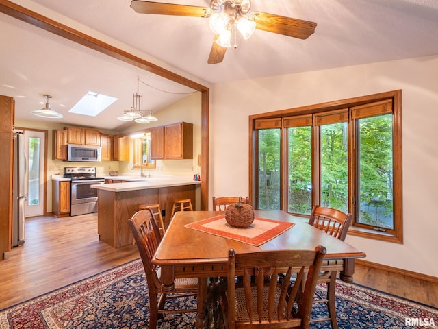 dining room featuring vaulted ceiling with skylight, light hardwood / wood-style floors, and ceiling fan