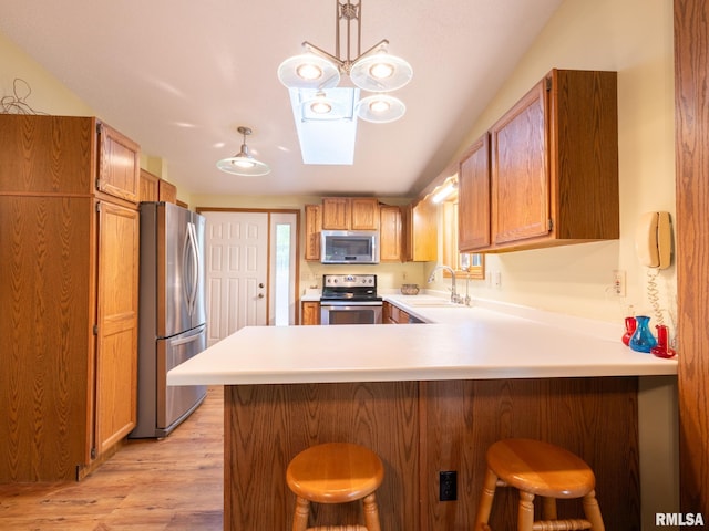 kitchen with pendant lighting, kitchen peninsula, appliances with stainless steel finishes, a breakfast bar area, and light wood-type flooring