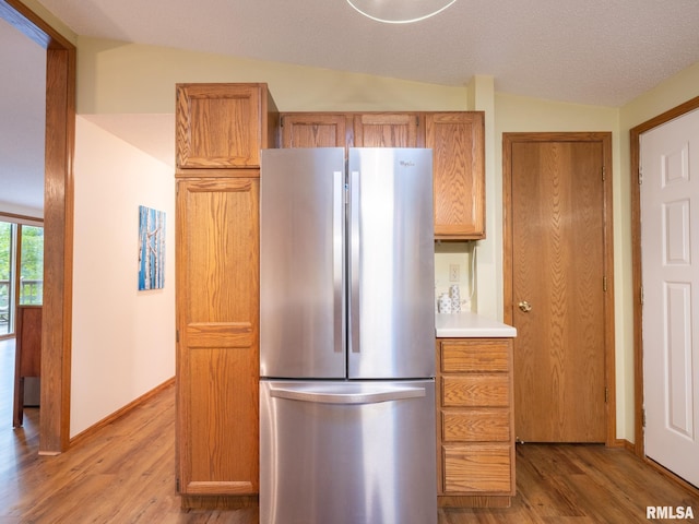 kitchen with light wood-type flooring, vaulted ceiling, and stainless steel refrigerator