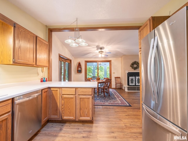 kitchen with decorative light fixtures, stainless steel appliances, light wood-type flooring, and kitchen peninsula