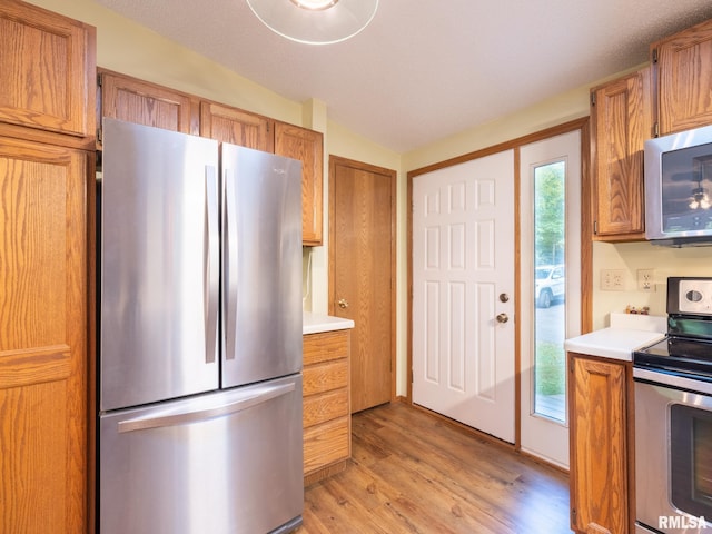 kitchen featuring a textured ceiling, appliances with stainless steel finishes, light hardwood / wood-style floors, and lofted ceiling