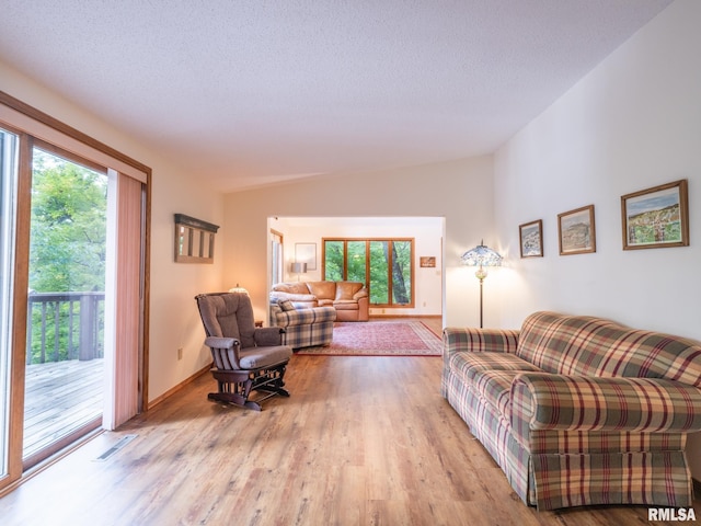 living room with a textured ceiling, lofted ceiling, light hardwood / wood-style flooring, and a wealth of natural light