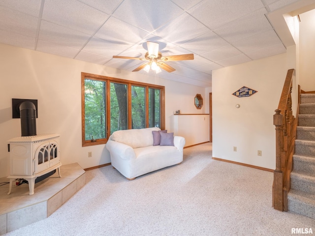 living room featuring ceiling fan, light carpet, a wood stove, and a paneled ceiling