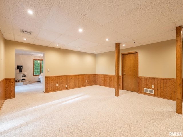 carpeted empty room with a drop ceiling and wooden walls