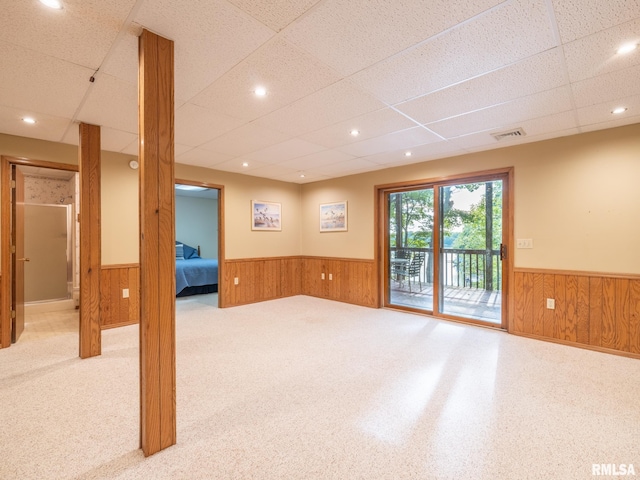 carpeted spare room featuring wooden walls and a paneled ceiling