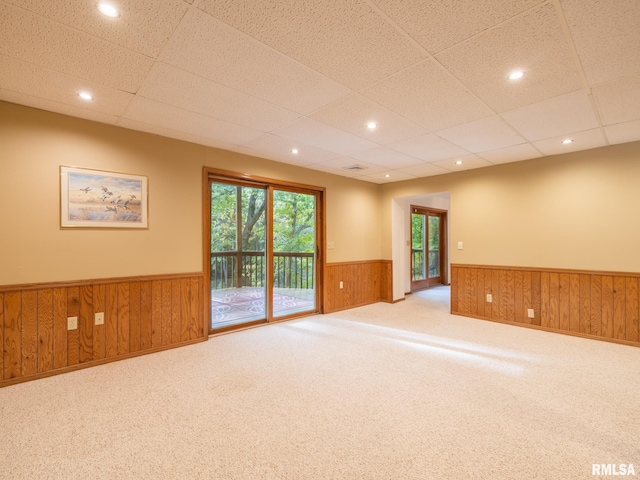 carpeted spare room featuring wooden walls and a drop ceiling