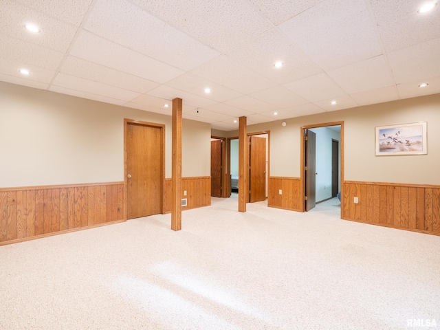 unfurnished room featuring a paneled ceiling, wood walls, and light colored carpet