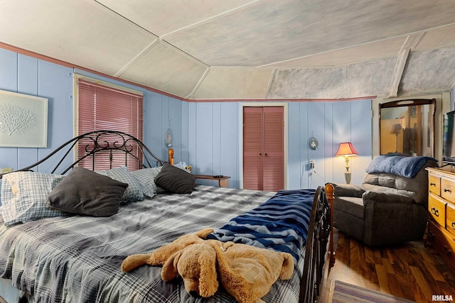 bedroom featuring wood-type flooring, wood walls, a closet, and vaulted ceiling