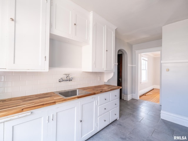 kitchen featuring wood counters, sink, white cabinets, decorative backsplash, and light hardwood / wood-style flooring