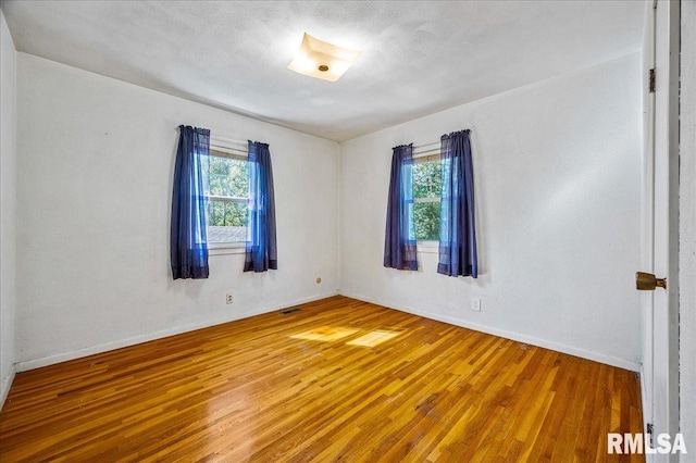 spare room featuring a textured ceiling, a healthy amount of sunlight, and hardwood / wood-style floors