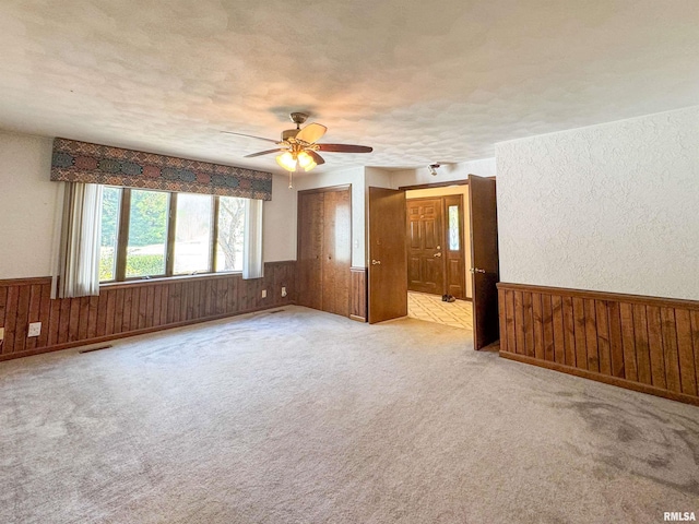 carpeted empty room featuring a textured ceiling, wood walls, and ceiling fan