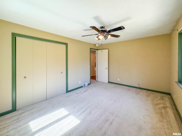 unfurnished bedroom featuring ceiling fan, light colored carpet, a textured ceiling, and a closet