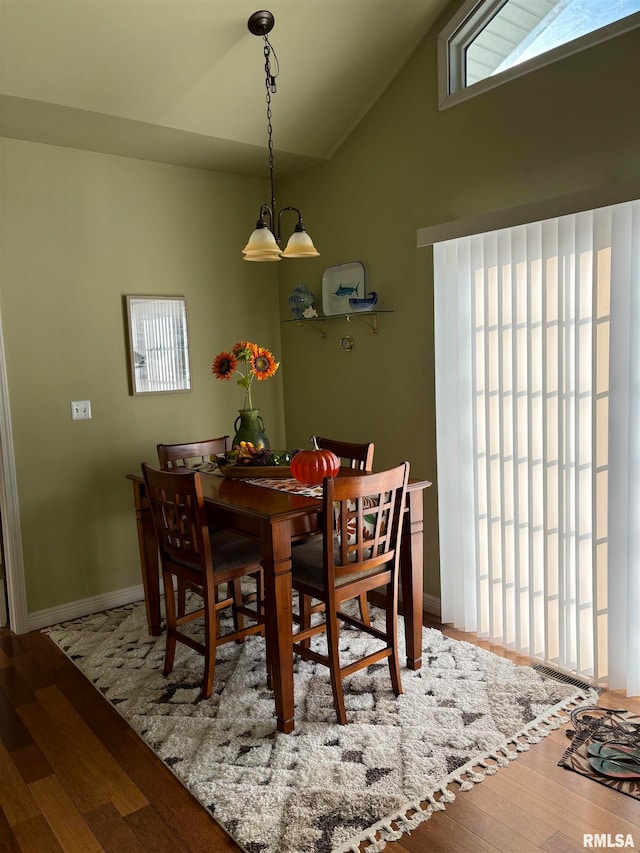 dining area featuring hardwood / wood-style flooring, a notable chandelier, and high vaulted ceiling