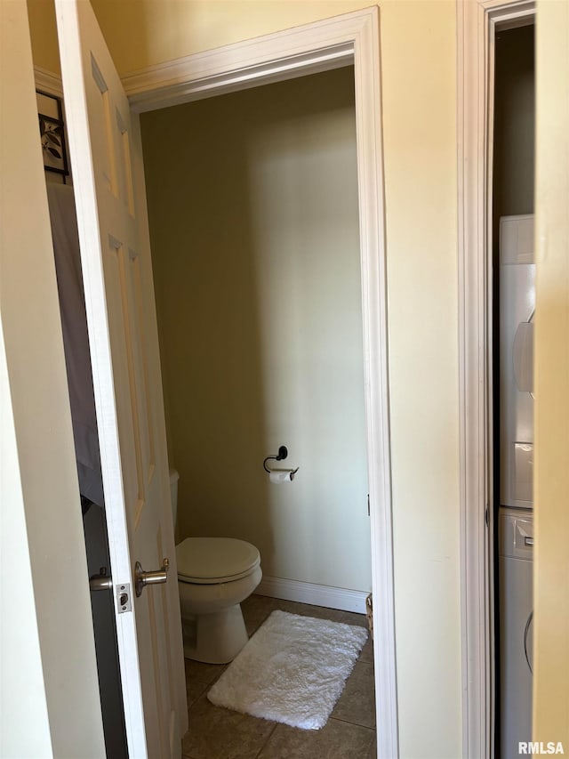 bathroom featuring stacked washer and clothes dryer, tile patterned flooring, and toilet