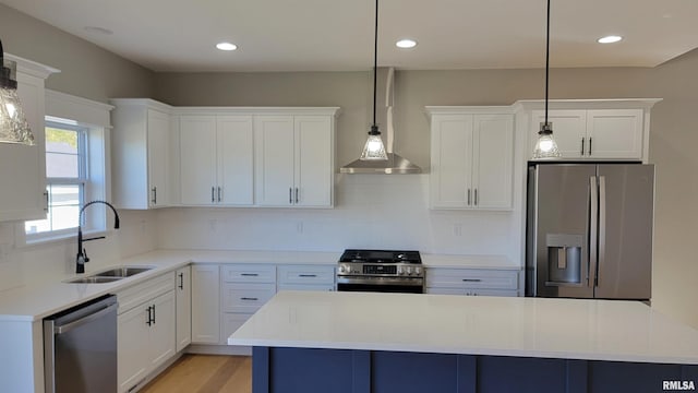 kitchen featuring white cabinetry, sink, wall chimney range hood, decorative light fixtures, and stainless steel appliances