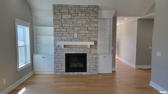 unfurnished living room with built in shelves, vaulted ceiling, light wood-type flooring, and a fireplace