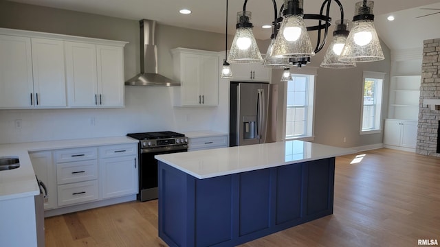 kitchen with appliances with stainless steel finishes, white cabinetry, hanging light fixtures, a kitchen island, and wall chimney exhaust hood