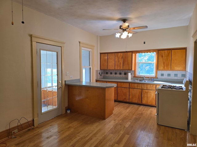 kitchen featuring sink, gas range gas stove, kitchen peninsula, light hardwood / wood-style flooring, and backsplash