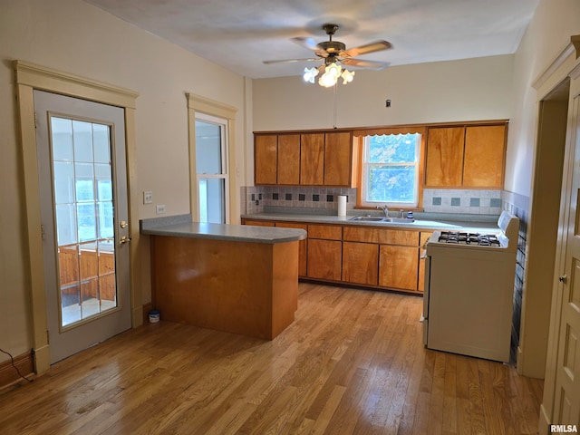 kitchen featuring light wood-type flooring, sink, kitchen peninsula, white range oven, and backsplash