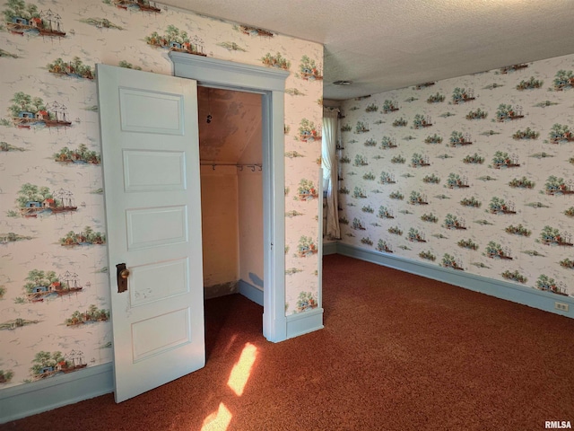 unfurnished bedroom with dark colored carpet, a spacious closet, a closet, and a textured ceiling