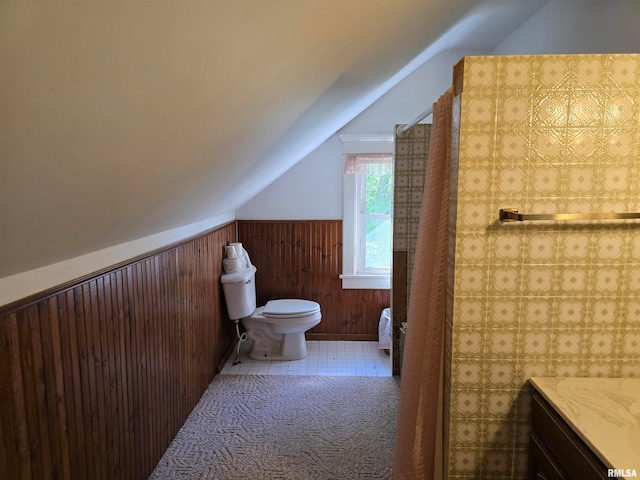 bathroom with lofted ceiling, wooden walls, vanity, and toilet