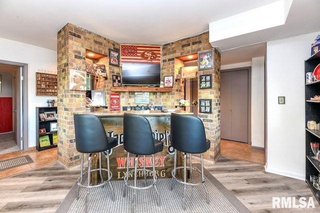 bar featuring hardwood / wood-style floors and brick wall