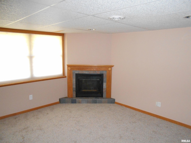 unfurnished living room with carpet floors, a drop ceiling, and a tiled fireplace