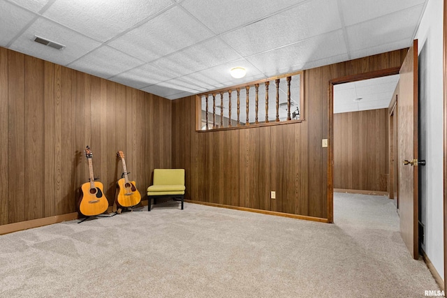 unfurnished room featuring a drop ceiling, light colored carpet, and wooden walls