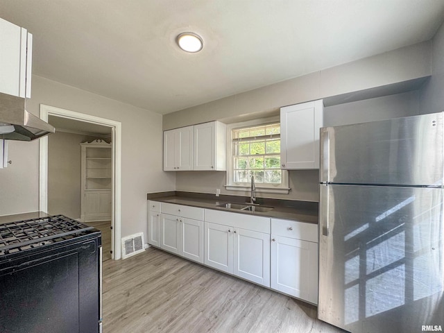 kitchen with white cabinets, stainless steel fridge, sink, light wood-type flooring, and black stove