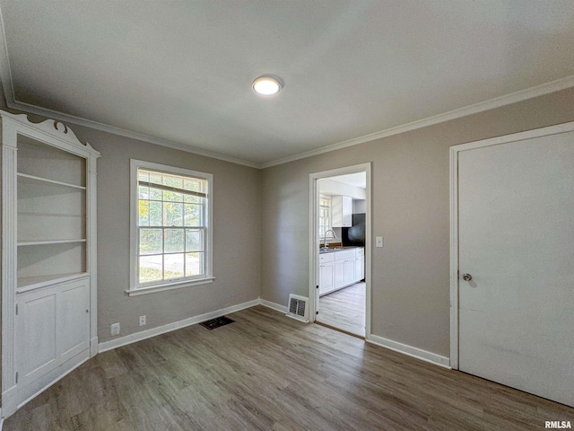 empty room with ornamental molding, sink, and wood-type flooring