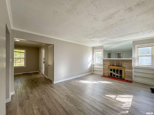 unfurnished living room with wood-type flooring, a stone fireplace, a textured ceiling, and a healthy amount of sunlight