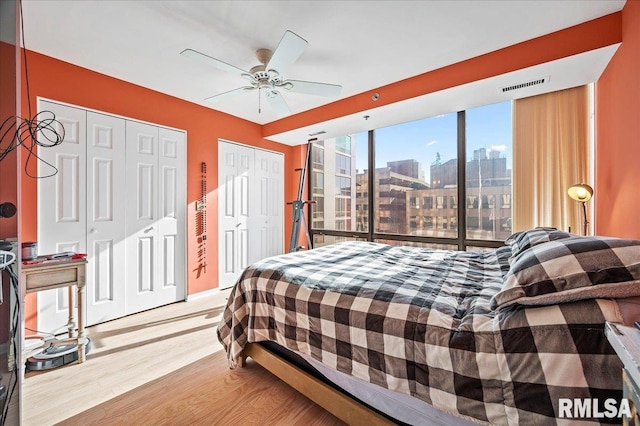 bedroom featuring ceiling fan, wood-type flooring, and two closets