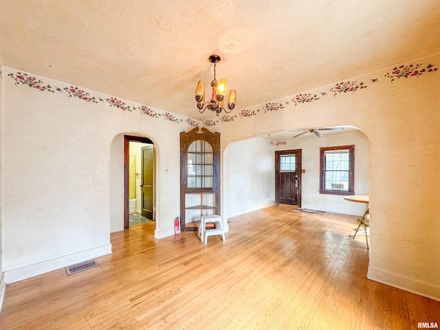 empty room featuring ceiling fan with notable chandelier, hardwood / wood-style flooring, and a textured ceiling