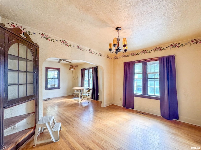 spare room with wood-type flooring, ceiling fan with notable chandelier, a textured ceiling, and a healthy amount of sunlight