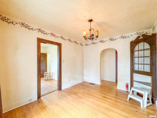 empty room featuring hardwood / wood-style floors, a chandelier, and a textured ceiling