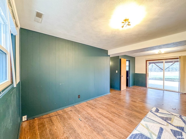 empty room with wood walls, light hardwood / wood-style flooring, and a textured ceiling