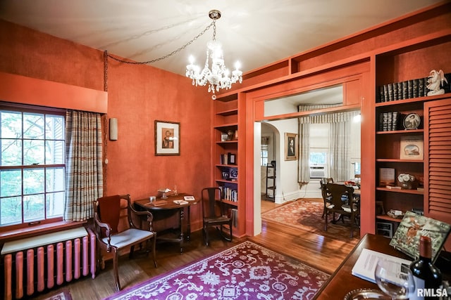 living area featuring wood-type flooring, cooling unit, radiator, an inviting chandelier, and built in shelves