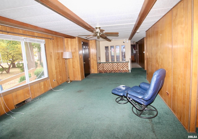 sitting room featuring wood walls, beamed ceiling, ceiling fan, and carpet floors