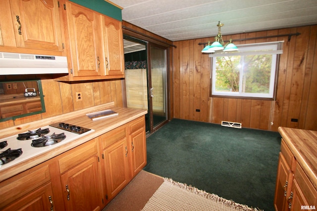 kitchen featuring wood walls, hanging light fixtures, dark colored carpet, and range hood