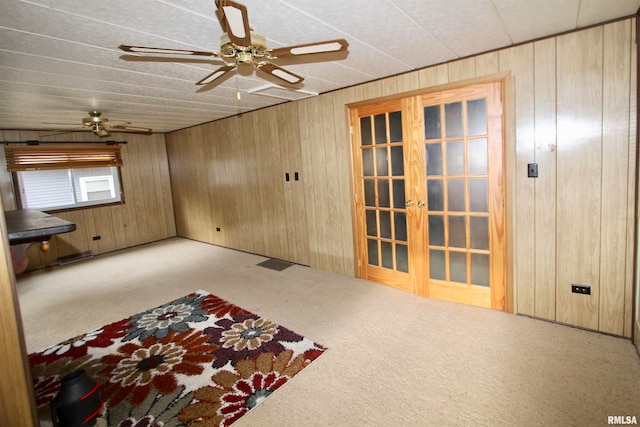 carpeted spare room featuring wood walls, ceiling fan, and french doors