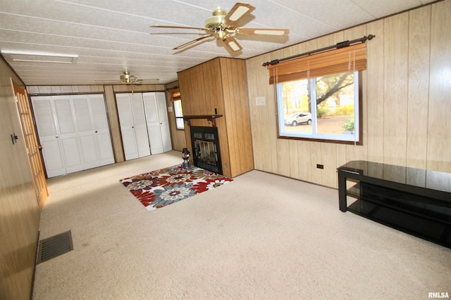 living room featuring ceiling fan, wooden walls, and light carpet