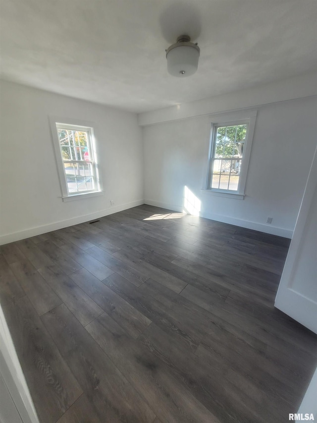 empty room with a wealth of natural light and dark hardwood / wood-style floors