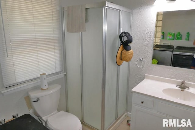 bathroom featuring a shower with door, vanity, washer and dryer, and toilet