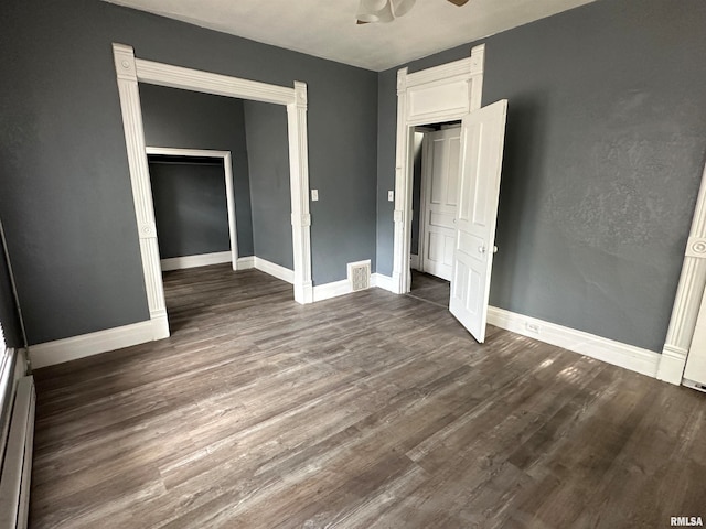 unfurnished bedroom featuring a closet, ceiling fan, a baseboard heating unit, and dark hardwood / wood-style floors