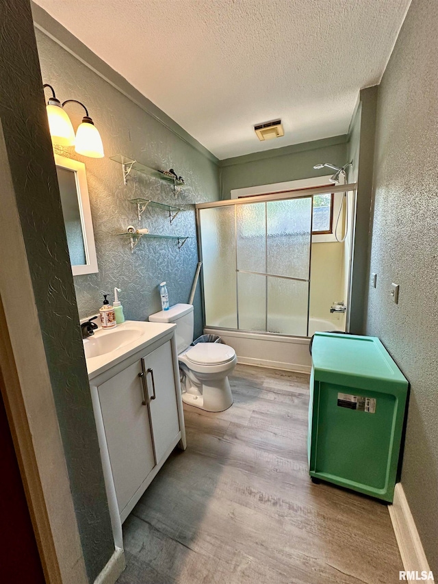 full bathroom with wood-type flooring, a textured ceiling, shower / bath combination with glass door, toilet, and vanity