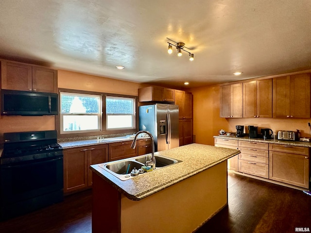 kitchen with appliances with stainless steel finishes, sink, an island with sink, dark hardwood / wood-style flooring, and light stone counters