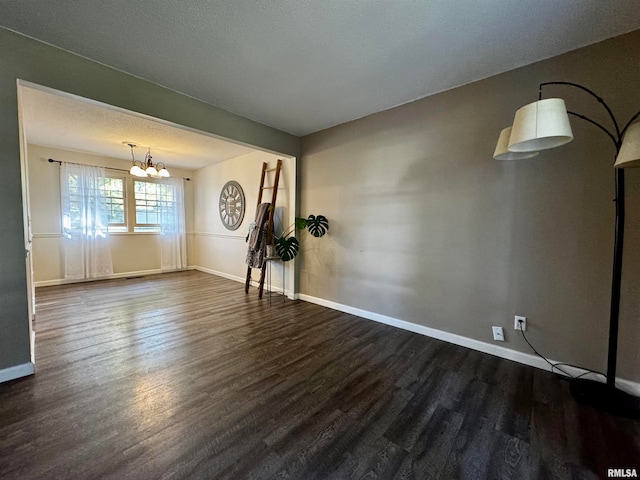 empty room with a textured ceiling, a chandelier, and dark wood-type flooring