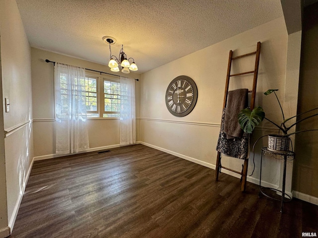 unfurnished dining area featuring dark wood-type flooring, a notable chandelier, and a textured ceiling