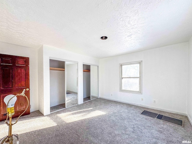 unfurnished bedroom featuring multiple closets, a textured ceiling, and carpet flooring