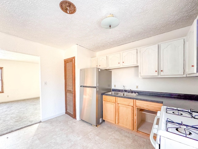 kitchen with sink, stainless steel refrigerator, white gas range oven, and white cabinetry